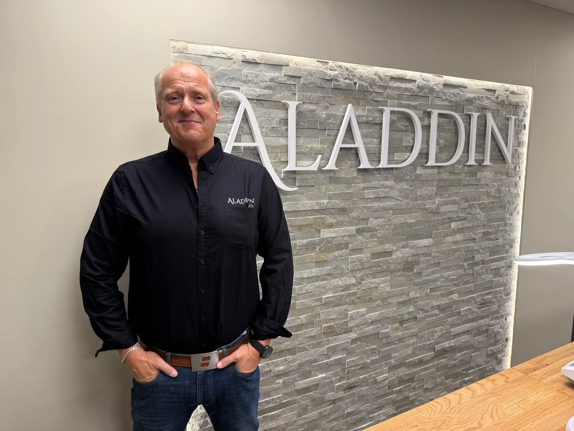 A man in a black shirt with an "ALADIN" logo stands by a stone wall with the large "ALADDIN" company name.