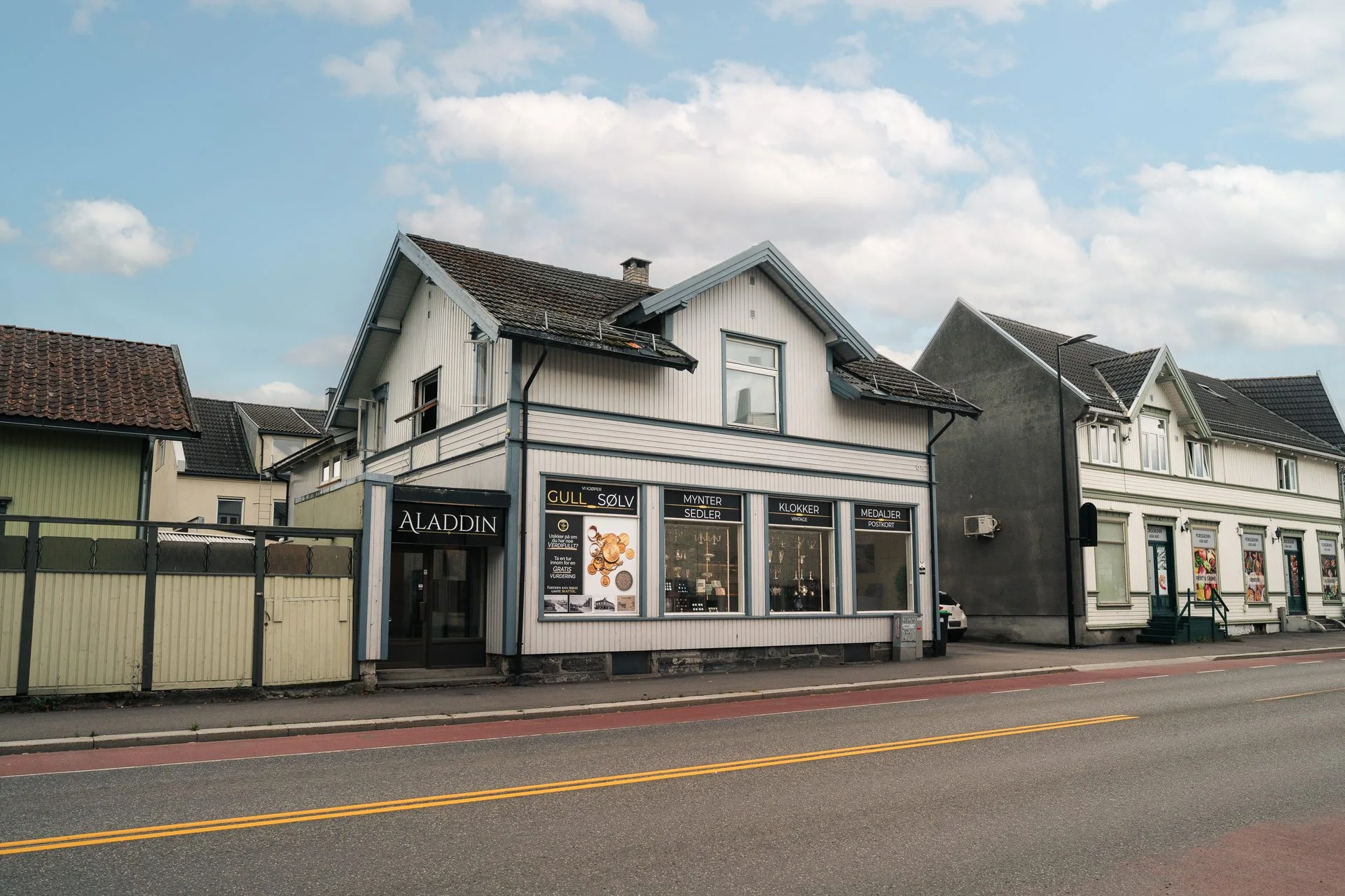 White commercial building named Aladdin on a street with other buildings and a road.