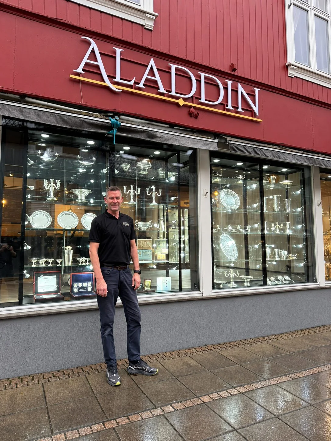 Man smiling in front of Aladdin store with silverware displays.